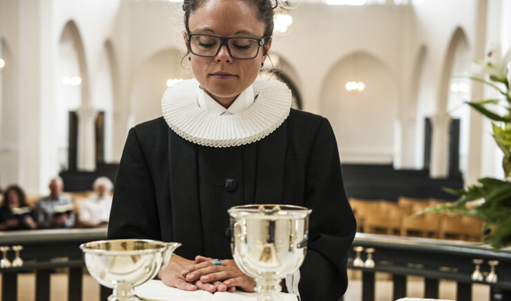 Præst står bag to alterkalke med hænderne på bibel