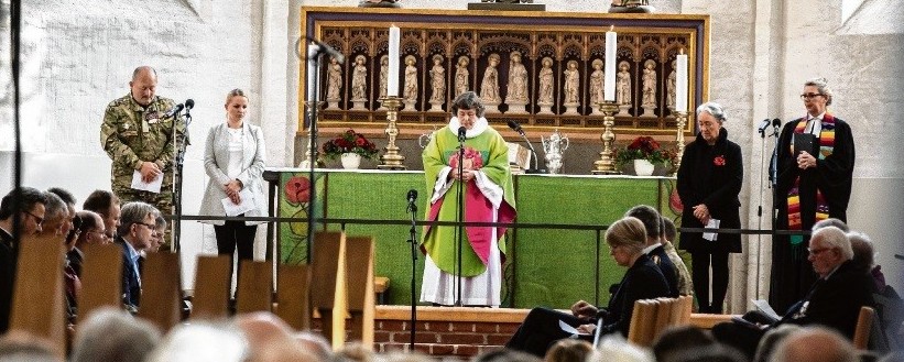 Biskop Marianne Christiansen står med tre kvinder og en mand i uniform ved alter foran mikrofoner